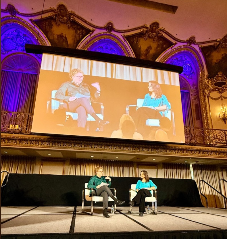 Joy Mayer and Monica Guzman on stage with a big screen behind them.